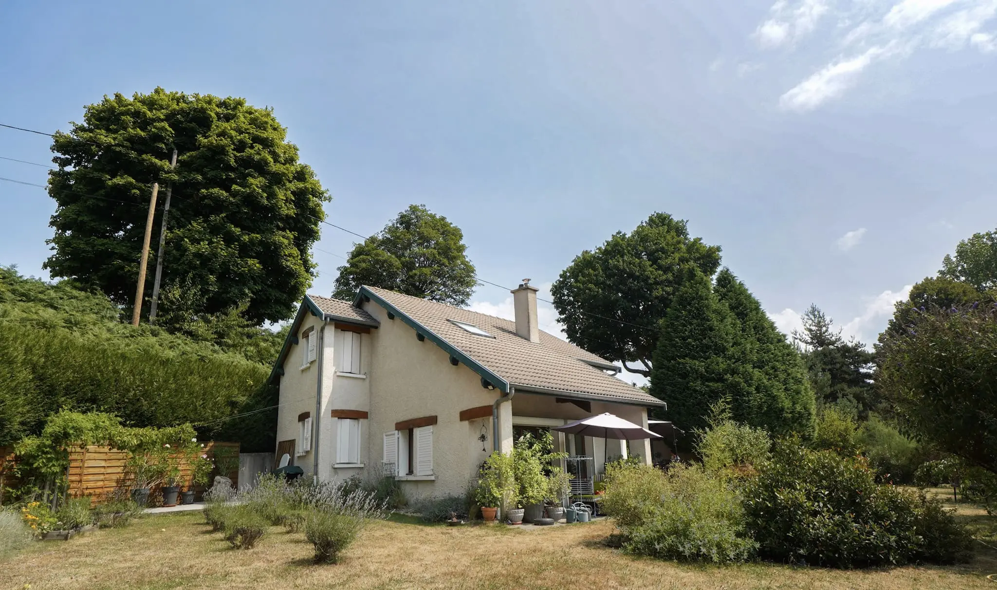 Maison individuelle avec jardin arboré et terrasse couverte, façade claire et toiture en tuiles, photographiée en été sous un ciel bleu – photographie immobilière Focus&Toit à Tournon-sur-Rhône.